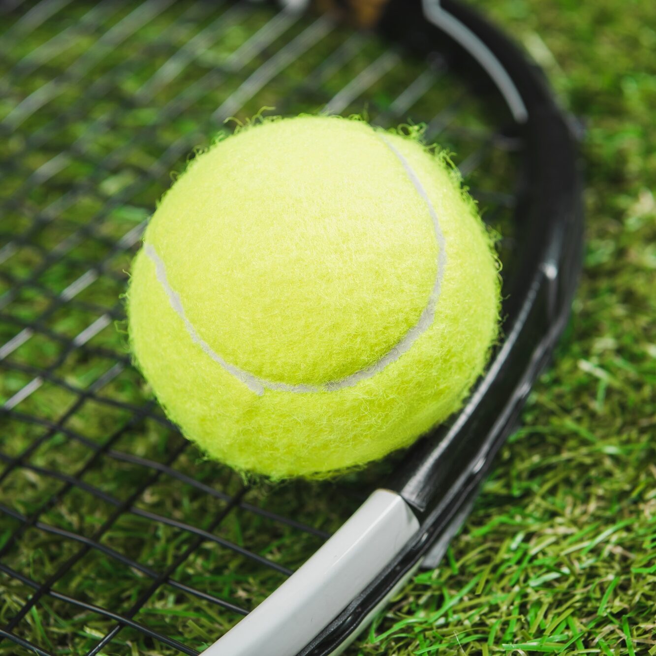 Close-up view of tennis racquet and ball on green grass